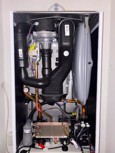 Inside of a combi boiler with the casing off, the ribbed metal plate heat exchanger visible at the bottom